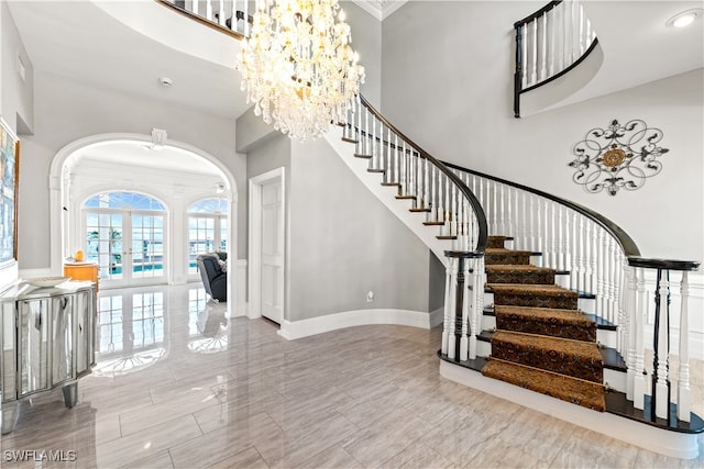 staircase with a towering ceiling, ornamental molding, french doors, and a notable chandelier