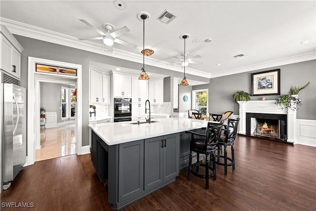 kitchen featuring hanging light fixtures, sink, oven, stainless steel refrigerator, and white cabinetry