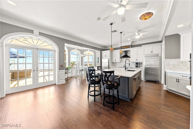 kitchen with dark hardwood / wood-style floors, stainless steel built in fridge, decorative light fixtures, a kitchen island with sink, and white cabinets