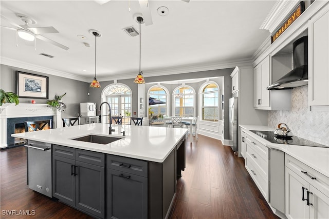 kitchen featuring a center island with sink, wall chimney range hood, pendant lighting, sink, and dark wood-type flooring