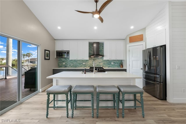 kitchen featuring white cabinetry, appliances with stainless steel finishes, light wood-type flooring, an island with sink, and wall chimney exhaust hood