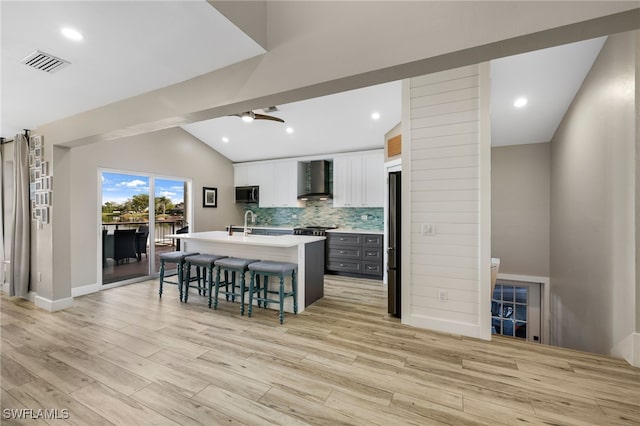 kitchen with a center island with sink, stainless steel appliances, white cabinets, a breakfast bar area, and wall chimney exhaust hood