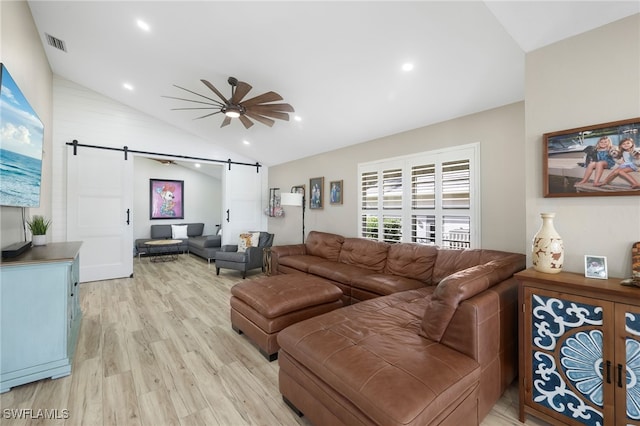 living room featuring light wood-type flooring, a barn door, ceiling fan, and vaulted ceiling