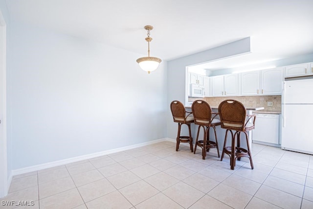 kitchen featuring pendant lighting, decorative backsplash, a breakfast bar, white cabinetry, and white appliances