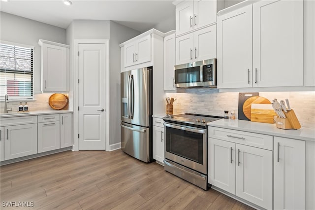 kitchen featuring sink, appliances with stainless steel finishes, light hardwood / wood-style flooring, white cabinets, and decorative backsplash