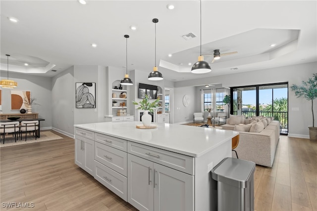 kitchen featuring light wood-type flooring, pendant lighting, a tray ceiling, ceiling fan, and a center island