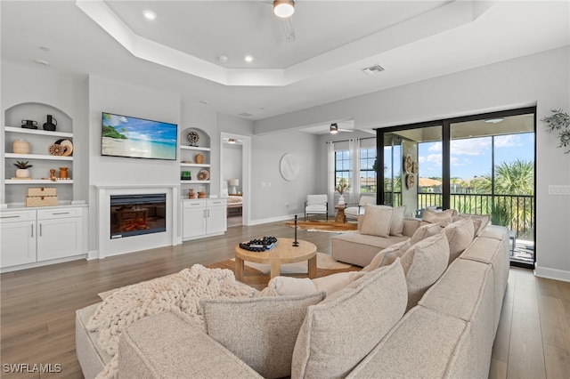 living room featuring built in features, hardwood / wood-style flooring, and a raised ceiling