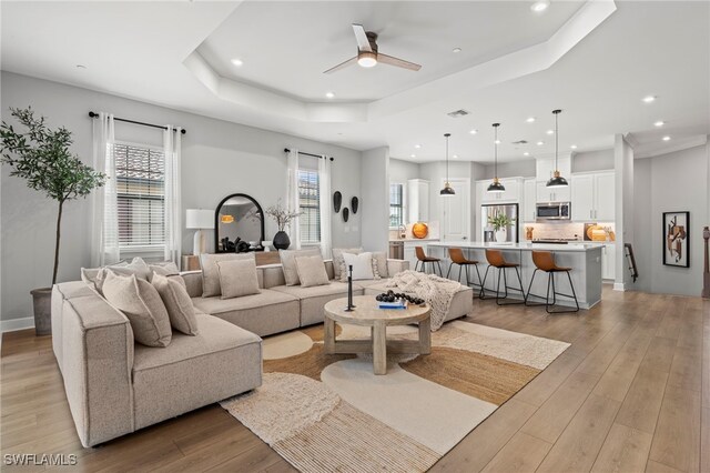 living room featuring ceiling fan, light hardwood / wood-style flooring, and a tray ceiling