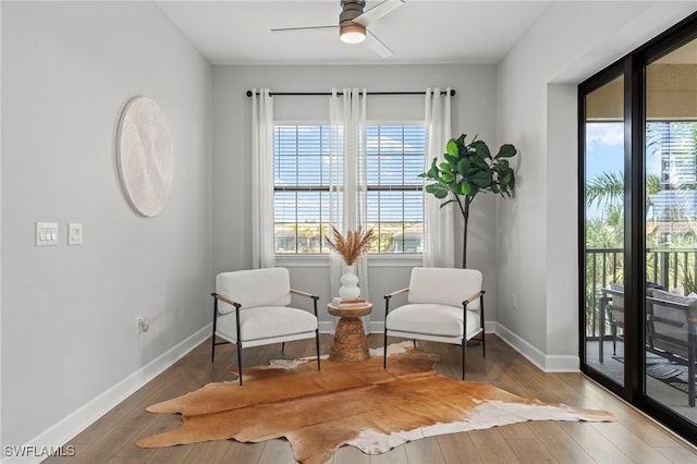 living area with a wealth of natural light, ceiling fan, and dark hardwood / wood-style flooring