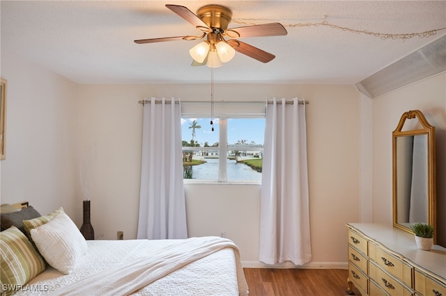 bedroom featuring ceiling fan, light hardwood / wood-style floors, vaulted ceiling, a textured ceiling, and a water view