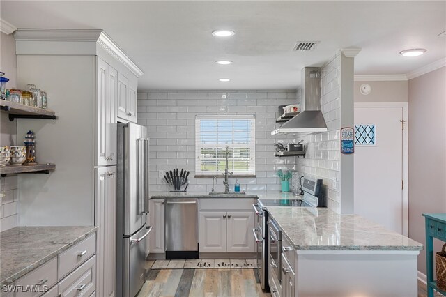 kitchen with wall chimney range hood, tasteful backsplash, light wood-type flooring, appliances with stainless steel finishes, and ornamental molding