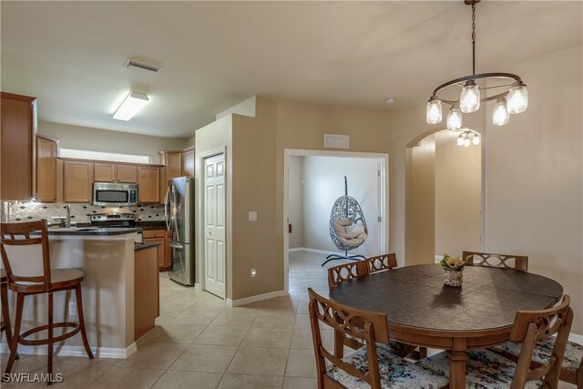 kitchen featuring stainless steel appliances, kitchen peninsula, light tile patterned floors, decorative light fixtures, and decorative backsplash