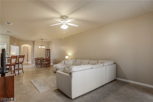 tiled living room with ceiling fan with notable chandelier