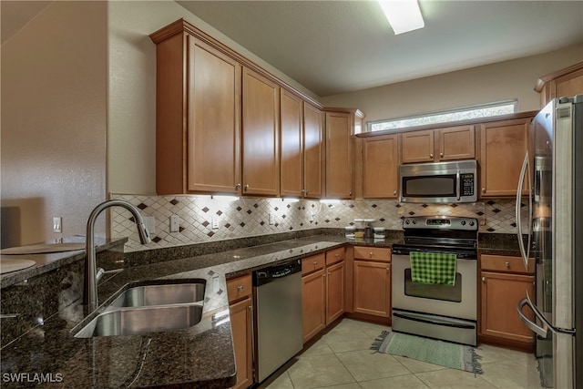 kitchen with stainless steel appliances, a sink, backsplash, dark stone counters, and brown cabinetry