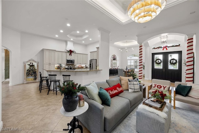 tiled living room featuring a notable chandelier, ornate columns, crown molding, and a tray ceiling