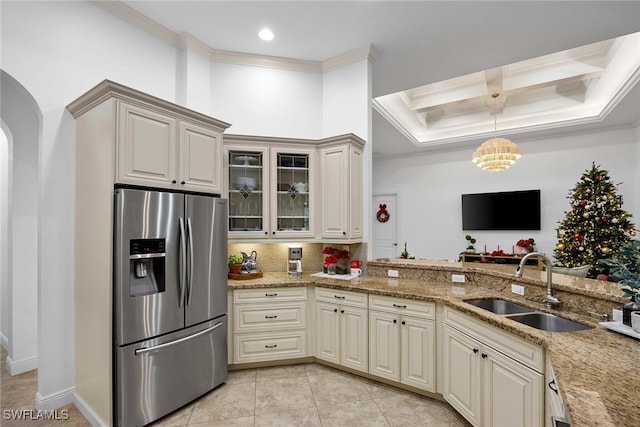 kitchen featuring sink, light stone counters, ornamental molding, stainless steel fridge, and pendant lighting