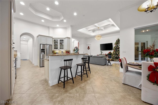 kitchen with light stone counters, stainless steel fridge with ice dispenser, a kitchen bar, a raised ceiling, and white cabinets