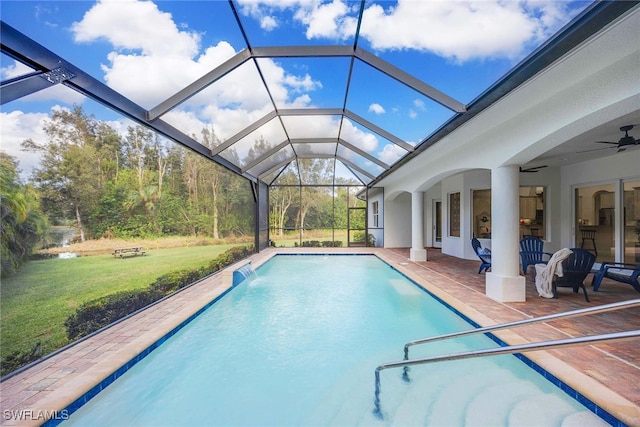 view of swimming pool featuring a patio area, ceiling fan, glass enclosure, pool water feature, and a yard