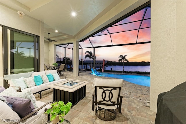 patio terrace at dusk with ceiling fan, a lanai, a water view, and an outdoor hangout area