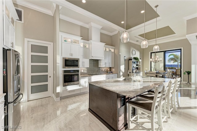 kitchen featuring light stone counters, decorative backsplash, an island with sink, white cabinetry, and appliances with stainless steel finishes