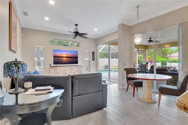 living room with ceiling fan with notable chandelier, light hardwood / wood-style floors, and crown molding