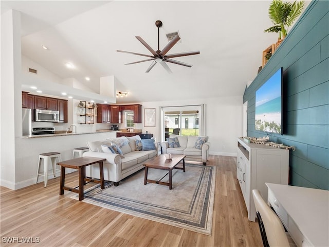 living room with ceiling fan, sink, light hardwood / wood-style flooring, and high vaulted ceiling