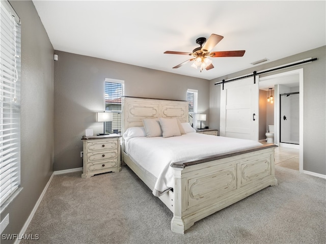 bedroom with ceiling fan, a barn door, light colored carpet, and ensuite bath