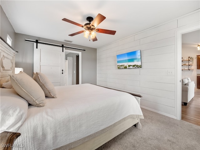 carpeted bedroom with ceiling fan and a barn door