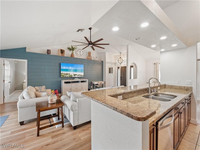 kitchen featuring stainless steel dishwasher, vaulted ceiling, sink, and light stone counters