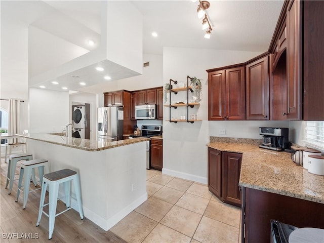 kitchen with stainless steel appliances, lofted ceiling, stacked washer / dryer, light stone countertops, and a breakfast bar