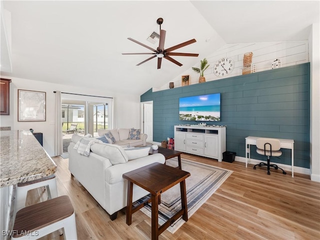 living room with light wood-type flooring, ceiling fan, lofted ceiling, and wooden walls