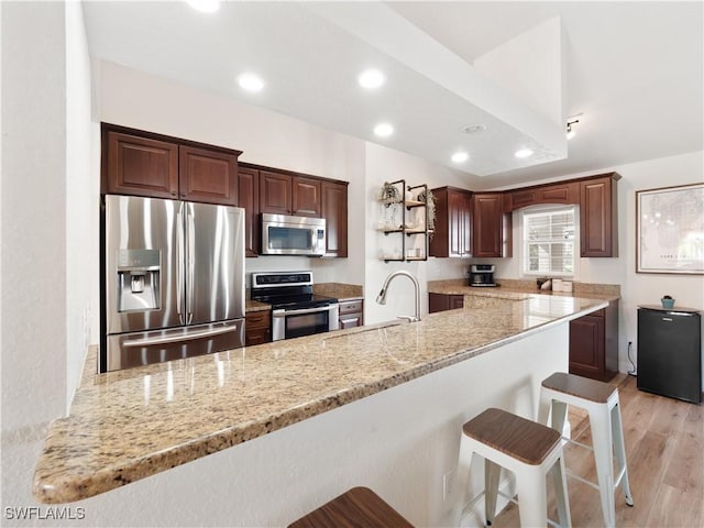 kitchen with light hardwood / wood-style floors, kitchen peninsula, stainless steel appliances, a kitchen breakfast bar, and light stone countertops