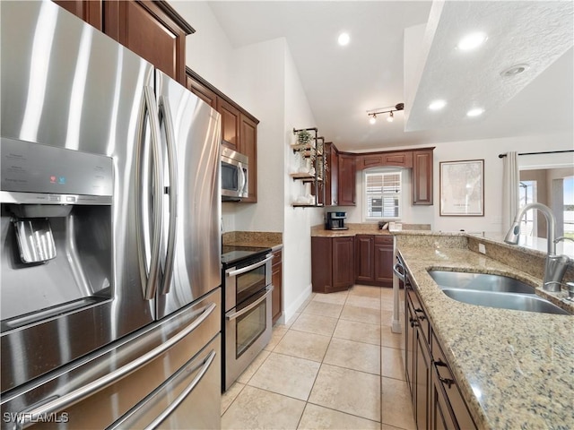 kitchen with sink, light stone countertops, appliances with stainless steel finishes, track lighting, and light tile patterned floors