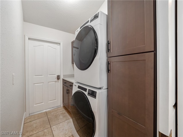 washroom featuring cabinets, stacked washer / dryer, a textured ceiling, and light tile patterned flooring