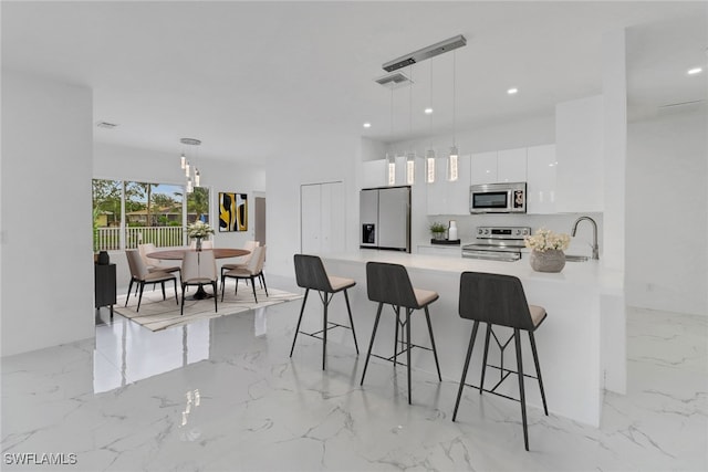 kitchen featuring kitchen peninsula, appliances with stainless steel finishes, a kitchen bar, decorative light fixtures, and white cabinets