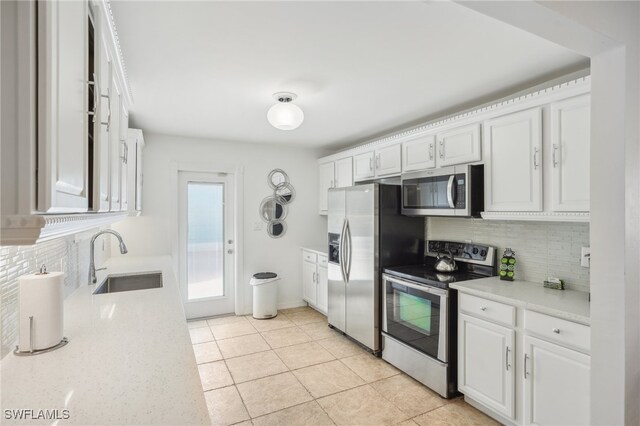 kitchen with stainless steel appliances, light stone counters, white cabinets, sink, and tasteful backsplash