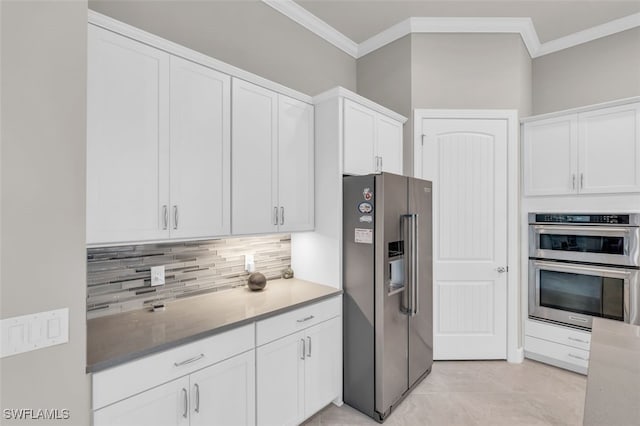 kitchen with appliances with stainless steel finishes, backsplash, ornamental molding, light tile patterned floors, and white cabinets