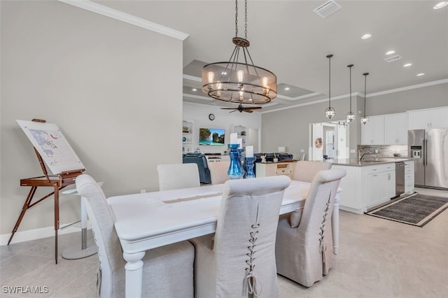 tiled dining area featuring ceiling fan with notable chandelier, a tray ceiling, ornamental molding, and sink