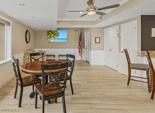 dining space with light hardwood / wood-style flooring, ceiling fan, and a tray ceiling