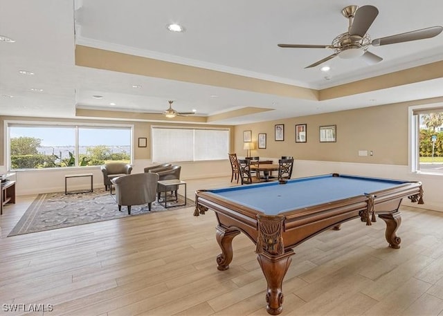 recreation room with ornamental molding, light wood-type flooring, and a tray ceiling