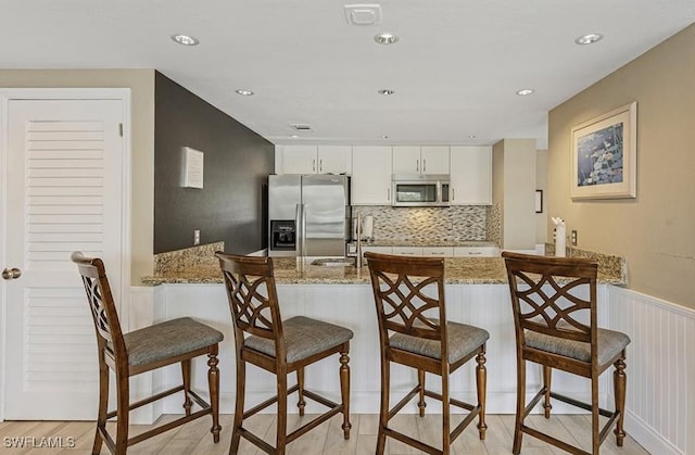 kitchen featuring light stone counters, stainless steel appliances, white cabinetry, kitchen peninsula, and light hardwood / wood-style flooring