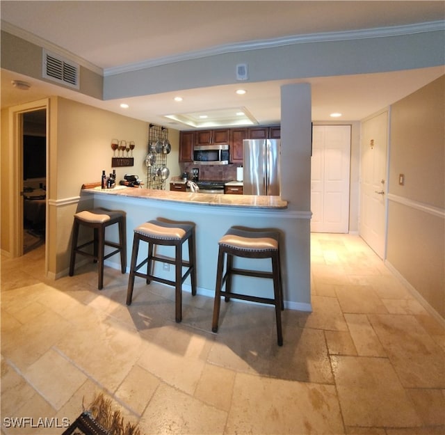 kitchen with a kitchen bar, kitchen peninsula, tasteful backsplash, crown molding, and appliances with stainless steel finishes