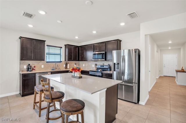 kitchen with stainless steel appliances, sink, a kitchen bar, a kitchen island, and decorative backsplash