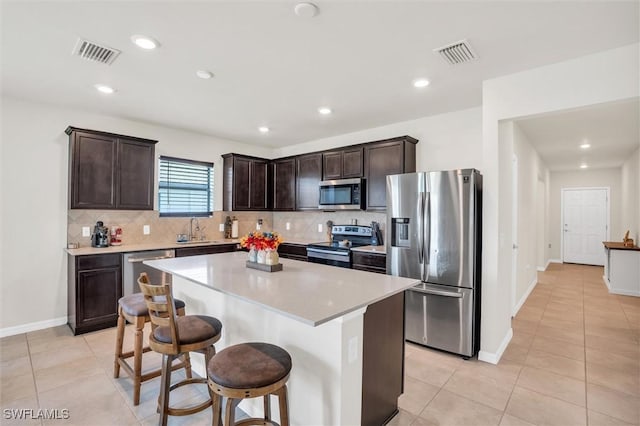 10852 Marlberry Way N, Fort Myers, FL 33917 - kitchen with stainless steel appliances, a sink, dark brown cabinetry, backsplash, and a center island