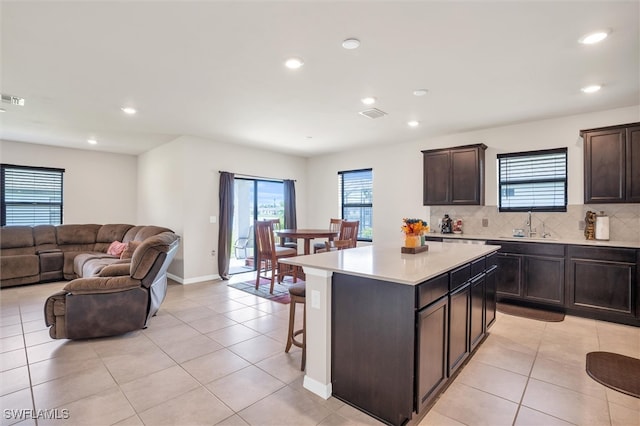 kitchen with a kitchen island, backsplash, a kitchen bar, dark brown cabinetry, and light tile patterned floors