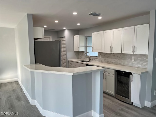 kitchen with sink, white cabinets, light hardwood / wood-style flooring, stainless steel refrigerator, and wine cooler