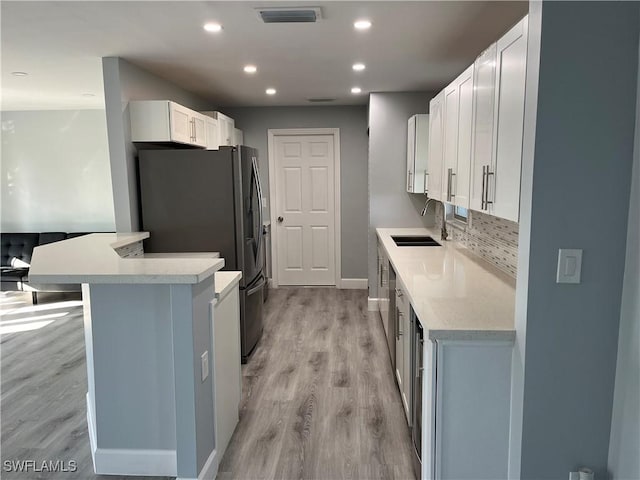 kitchen with stainless steel refrigerator with ice dispenser, white cabinetry, light hardwood / wood-style floors, and sink