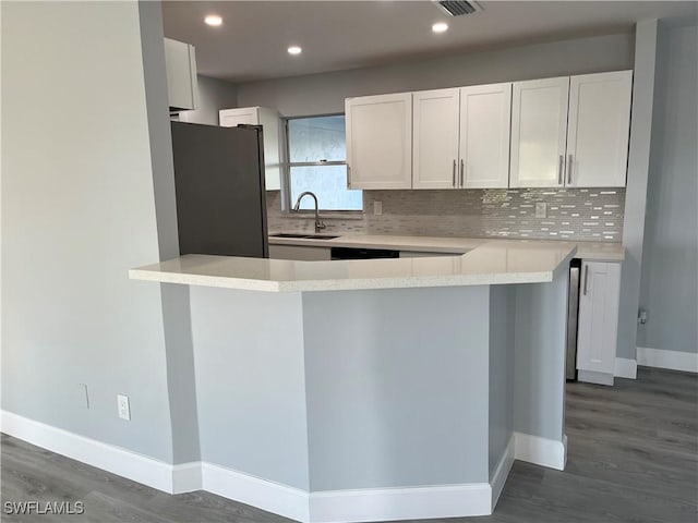 kitchen featuring stainless steel refrigerator, kitchen peninsula, sink, white cabinets, and tasteful backsplash