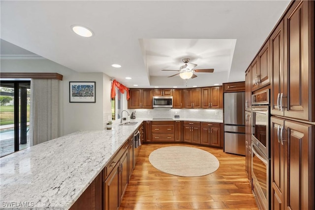 kitchen featuring light stone countertops, sink, ceiling fan, a tray ceiling, and appliances with stainless steel finishes