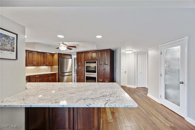 kitchen featuring decorative backsplash, a peninsula, light stone countertops, stainless steel appliances, and light wood-style floors